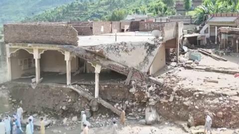 Debris from a partially destroyed home falls from a bank carved in the earth from flood waters.