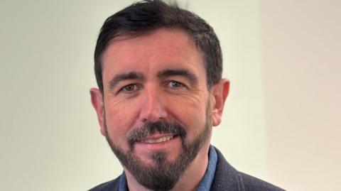 Paul Doherty, a man with dark hair and a beard, wearing a dark jacket and blue shirt.