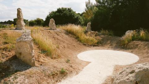 A chalk pathway leads to the centre right of the image and goes into a circle. Around it is a grass verge and chalk stones. 