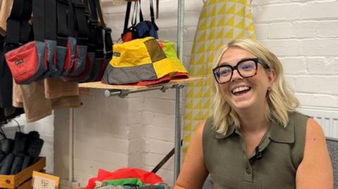 A woman smiling with a clothes rack behind her