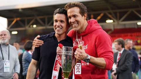 Wrexham co-owners McElhenney (left) and Ryan Reynolds (right) hold a League One promotion trophy
