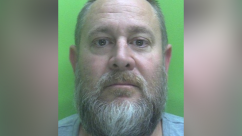 Custody photo of Neil Piggott with beard and wearing grey t-shirt