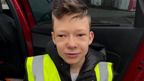 A young boy with brown hair is wearing a hi-vis jacket.