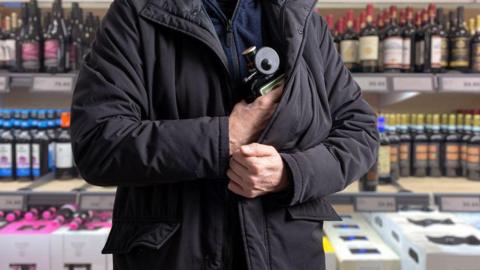 A person concealing a bottle of alcohol in the black jacket they are wearing,