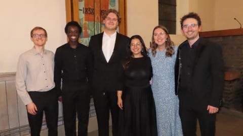 Six members of the Warrington Musical Society at the final concert in a church. They are all smiling. Left to right: Ethan Mitchell (accompanist) Aaron Peters (tenor), Elliot Maxwell-Hodkinson (bass), Nia Edwards (alto), Katherine Macaulay (soprano) and Louis de Satgé (musical director).
