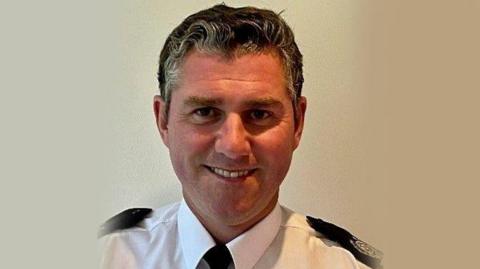 Stewart Forshaw smiles at the camera. He is wearing his uniform, including a white shirt and dark coloured tie.