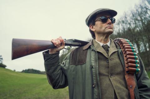 David Tennant in his role in the Disney+ series Rivals. He is wearing a tweed jacket, a cap, sunglasses and has a shotgun and ammunition slung over his shoulder