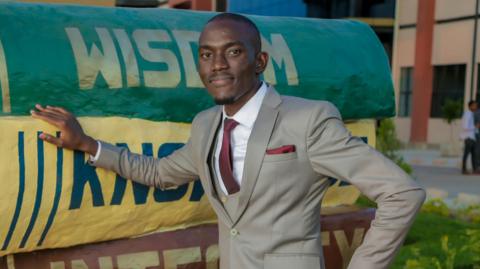 Malama Muleba poses wearing a grey, three-piece suit and red tie.