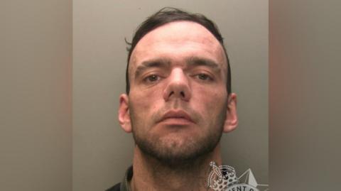 George Powell is shown in a police mugshot, looking at the camera. 