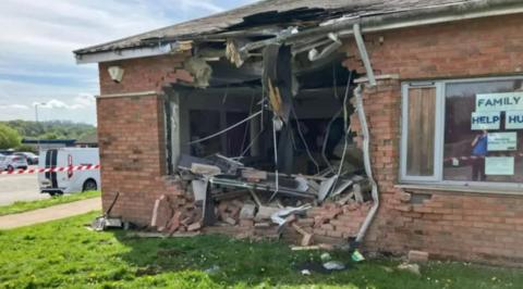 A one-storey brick building with a large hole knocked in one wall and red and white tape to the left