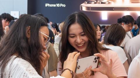 Two young women look at an iPhone 16 Pro at an Apple Store in Chengdu, China.