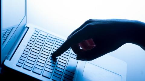 Silhouette of hand pressing keys on laptop keyboard.