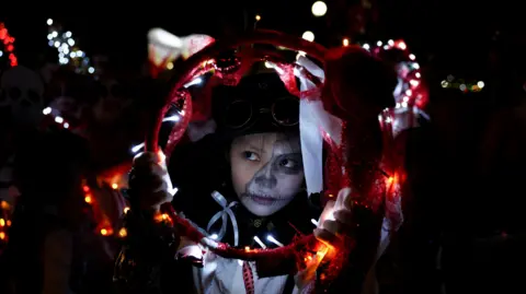 A child with face paint is holding a red circle with lights 