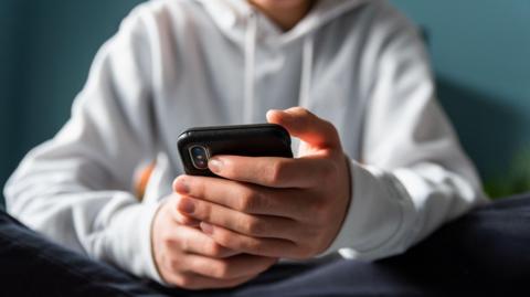 A generic image of a boy in a white hooded sweatshirt holding a mobile phone.