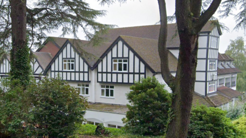 A black and white timbered building standing behind trees