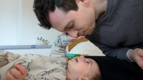 A man leans down and closes his eyes as his smiling baby reaches out to touch his face