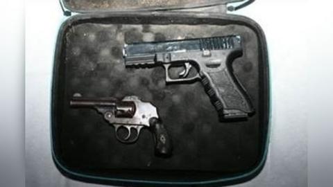 Two guns - a Glock-style pistol and a small vintage-looking enclosed-hammer revolver - lie in a small case which has black padding.