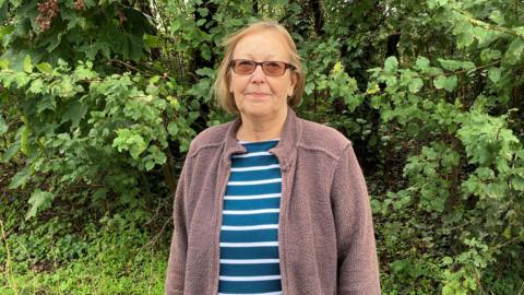 Head and shoulders picture of resident Susan Bell standing in front of a green bush