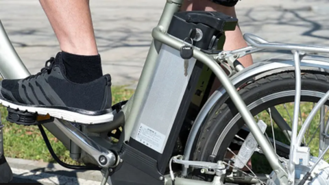 A close-up of a foot in a trainer, on the pedals of a silver e-bike