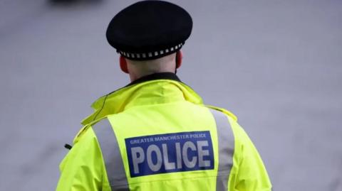 Greater Manchester Police officer in uniform including hi-vis jacket and helmet showing shaved head from behind