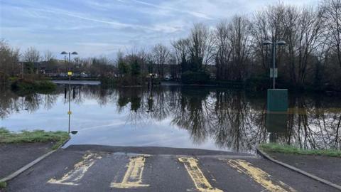 A river has burst its banks. The water can be seen creeping up on to a zebra crossing
