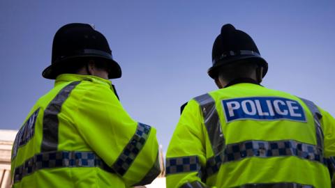 A generic image of two police officers standing with their backs to the camera. They are wearing high-visibility jackets with POLICE wording on the back