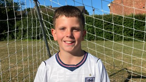 A child with an england jersey on standing in front of a goal