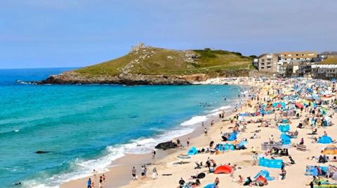 Blue skies and turquoise seas. Busy, sandy beach in Cornwall