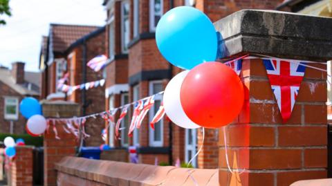 Red, white and blue balloons and union jack bunting on a brick house. 