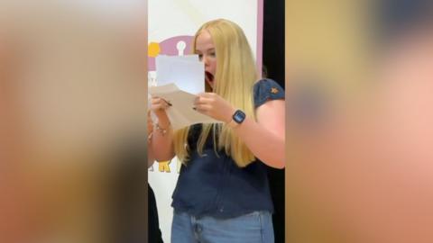 A blonde girl gasps while looking at a sheet of paper.