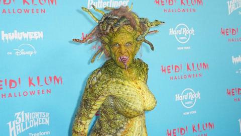 Model Heidi Klum is in a green slithering Medusa costume complete with moving snakes on her head and a snake-like tongue.