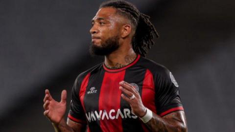 Crawley Town manager Colin Kazim-Richards in his plaing days wearing black and red vertical stripes of turkish side Fatih Karagumruk SK, holding hands up in front of his chest about to clap