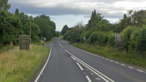 A google street view image of a flat, straight, dual carriageway with grass, trees and road signs either side.