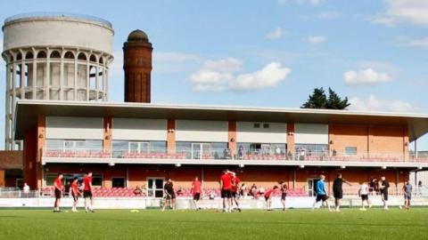 A coaching session taking place at Goole AFC's ground. There are several players on the pitch, The main stand is in the background and a water tower can be seen behind that.