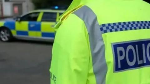 Generic shot of police officer in hi-vis jacket with police car in the background