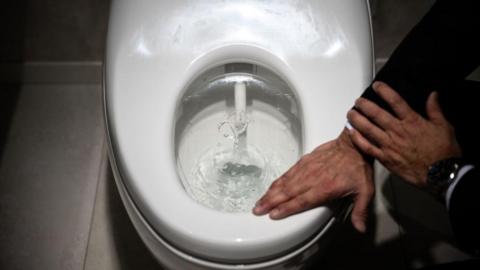 A man touching a Toto toilet seat with his hand