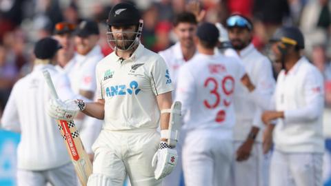 New Zealand batter Kane Williamson walks off after being dismissed as England players celebrate in the background