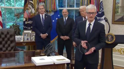 TIm Cook holds a glass disc with the Apple logo cut out in the centre, while President Trump looks on behind him.