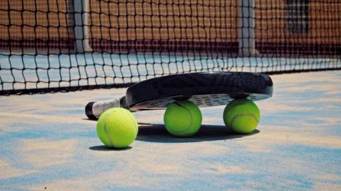 A padel racquet and balls on the floor next to a net