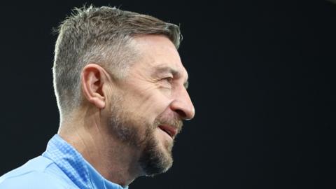 Port Vale manager Jon Brady facing side on while standing on the pitch before kick-off
