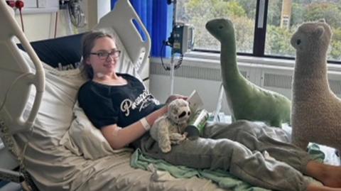 Eliana sits in a hospital bed with cuddly toys