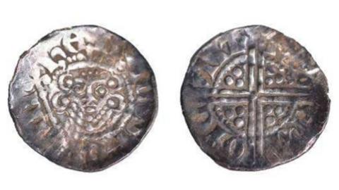 A silver Medieval coin photoaged from the front and back. The coin is shiny with a Celtic cross engraved on one side and a monarch's face on the other.