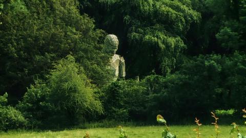 Image of a large robot statue half hidden behind trees in a field