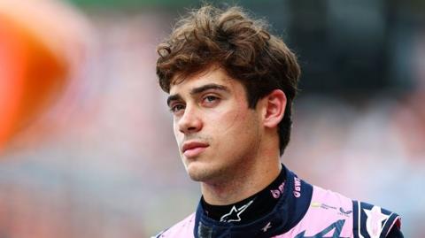 Alpine F1 driver Franco Colapinto, wearing a pink and blue race suit, looks on in the pit lane during qualifying for the 2026 Dutch Grand Prix