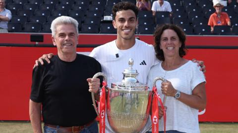 Francisco Cerundolo poses with the Queen's trophy alongside his parents