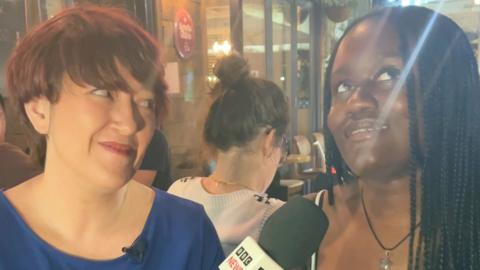 A reporter asks a question to a woman in a bar who looks indecisive