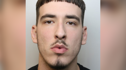 A mugshot of Oskar Krzeszewski. He has a small moustache and goatee and is wearing a black top.