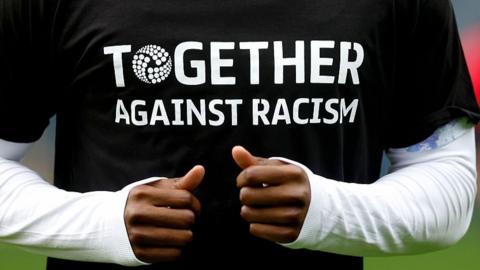 A footballer wears a 'Together Against Racism' during warm-ups