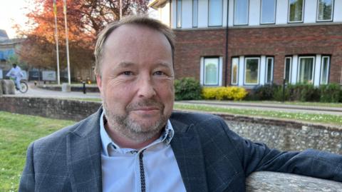 Man with short hair and beard sitting on bench outside council offices