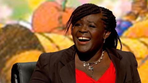 A head and shoulders shot of a smiling Dame Aderin-Pocock who is wearing a red dress and brown blazer.